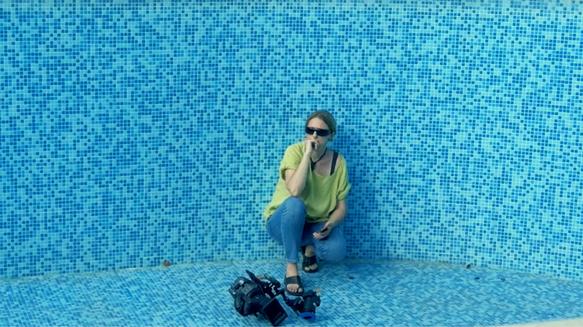 Georgia Mihalcea, filmmaker and creator of Semantic Filmmaking Method, sits introspectively in an empty blue-tiled swimming pool, symbolizing her exploration of 'numbness' and emotional detachment in art and life.